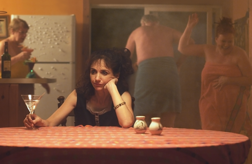 Edie McClurg and C. Fraser Press from Theresa is a Mother portray a woman sitting at a table with a mirror reflecting a man and another woman in a room.